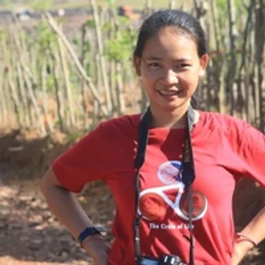 A woman wearing a red t-shirt standing in front of a field