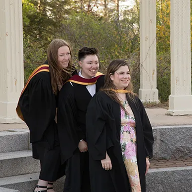 Students smiling outdoors wearing graduation gowns