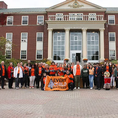 Students wearing orange with an Every Child Matters sign in front og George Martin Hall
