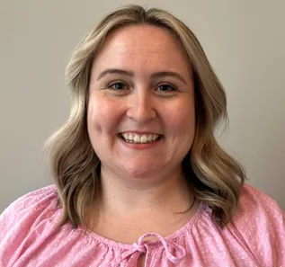 A woman with shoulder-length hair, wearing a pink top