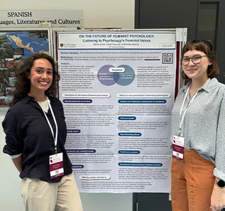 Two female STUdents smiling and standing next to poster at an academic conference