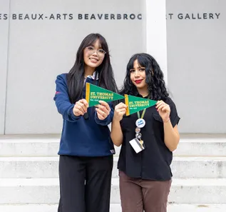 Laura Thai and Charlotte James at the Beaverbeook Art Gallery holding STU pennants