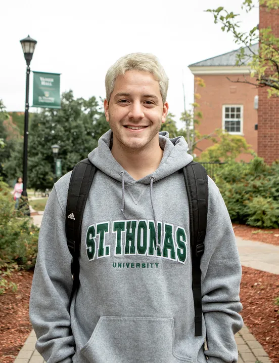 Photo of a male student with blond hair and a STU hoodie on campus with backpack