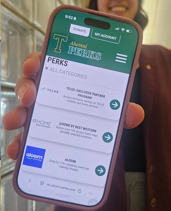 A close up of someone holding out their phone which is displaying the STU Alumni Perks page