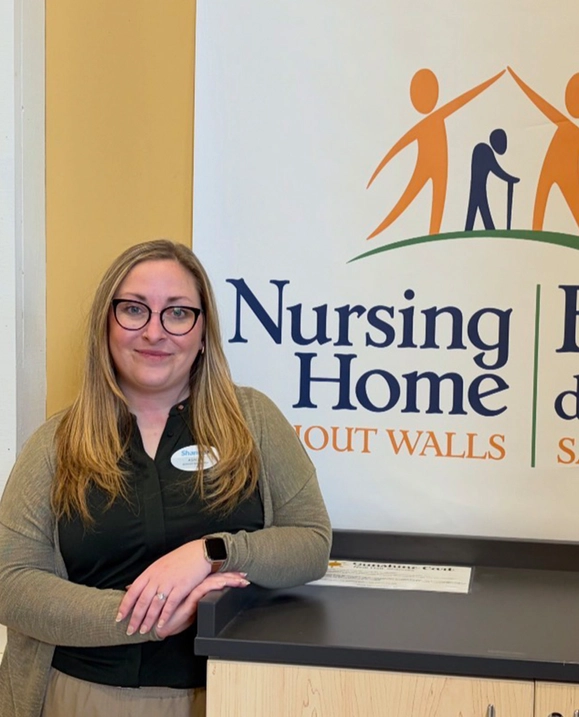 STU Alumna Ashley Erb stands in front of a Nursing Home Without Walls Sign
