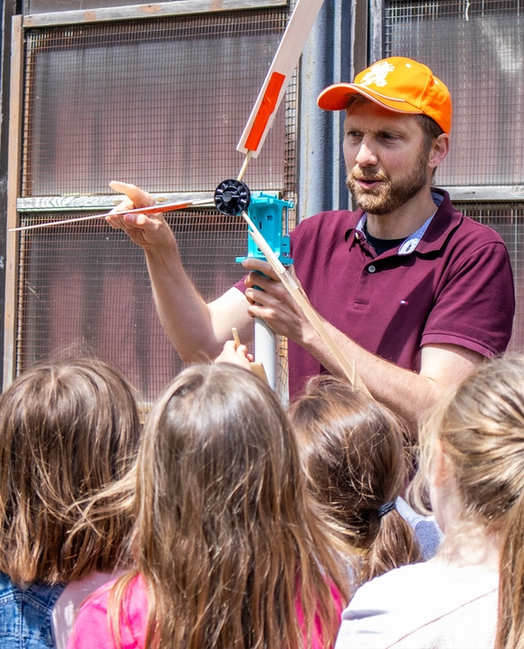 A male student demonstrates how a windmill works for a group of young children