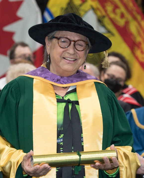 Honorary Degree recipient Maggie Paul stands with her cap and gown at Spring Conovcation 2022