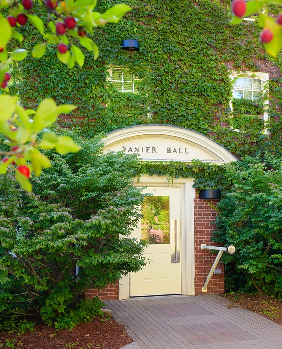 A brick building covered in green vines with the words Vanier Hall above the door