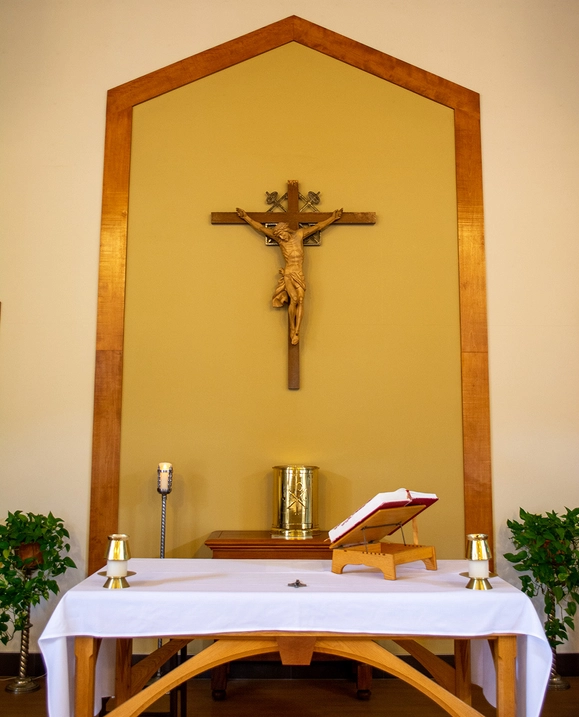 A crucifix hangs on the wall behind a table with candles and an open Bible.
