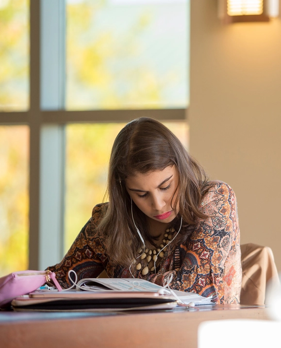 A female student sits at a table in study hall, reading a textbook