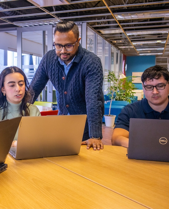 A female student and male student sit at a table while their internship supervisor speaks with them about their work