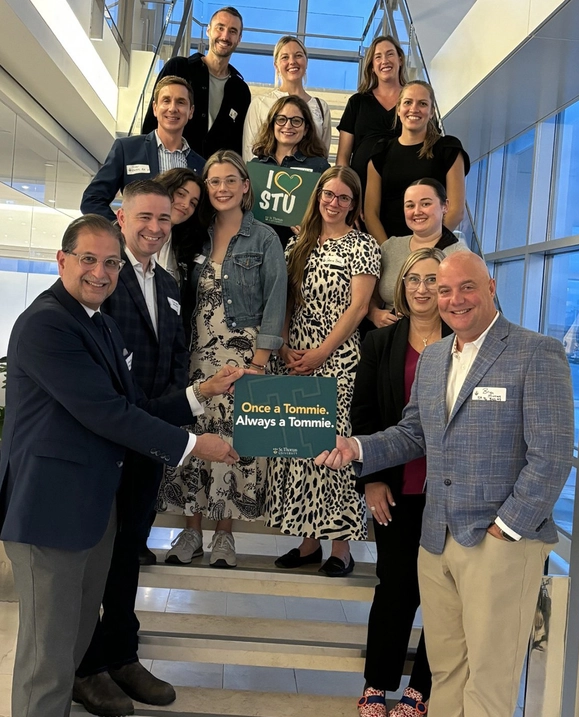 A group of STU alumni along with STU president Dr. Nauman Farooqi stand in a stairwell holding signs that read 