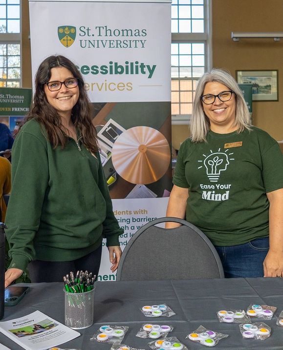 Two female employees stand in front of a banner that says 