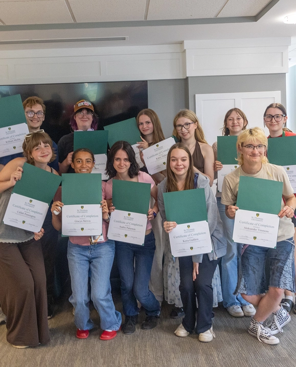 A group of students stand together in the student lounge holding their certificates of completion for the Rubin Depow Summer Study Program