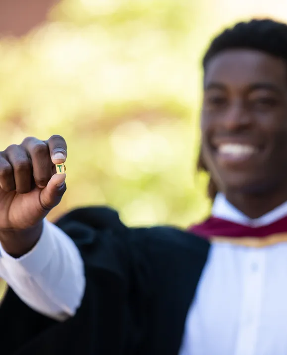 Grad holding up T-Pin in graduation gown