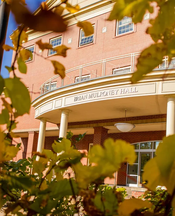 A close up of the sign on Brian Mulroney Hall, shot through fall leaves