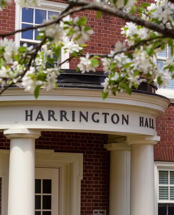 A photo of the Harrington Hall entrance and sign with spring blooms around it
