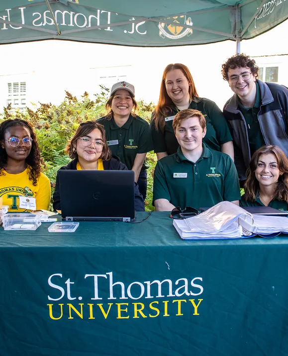 A group of Residence Team members smile together behind a table with a St. Thomas University table cloth