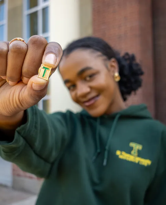 A female student holds out a gold T-Pin outside on campus