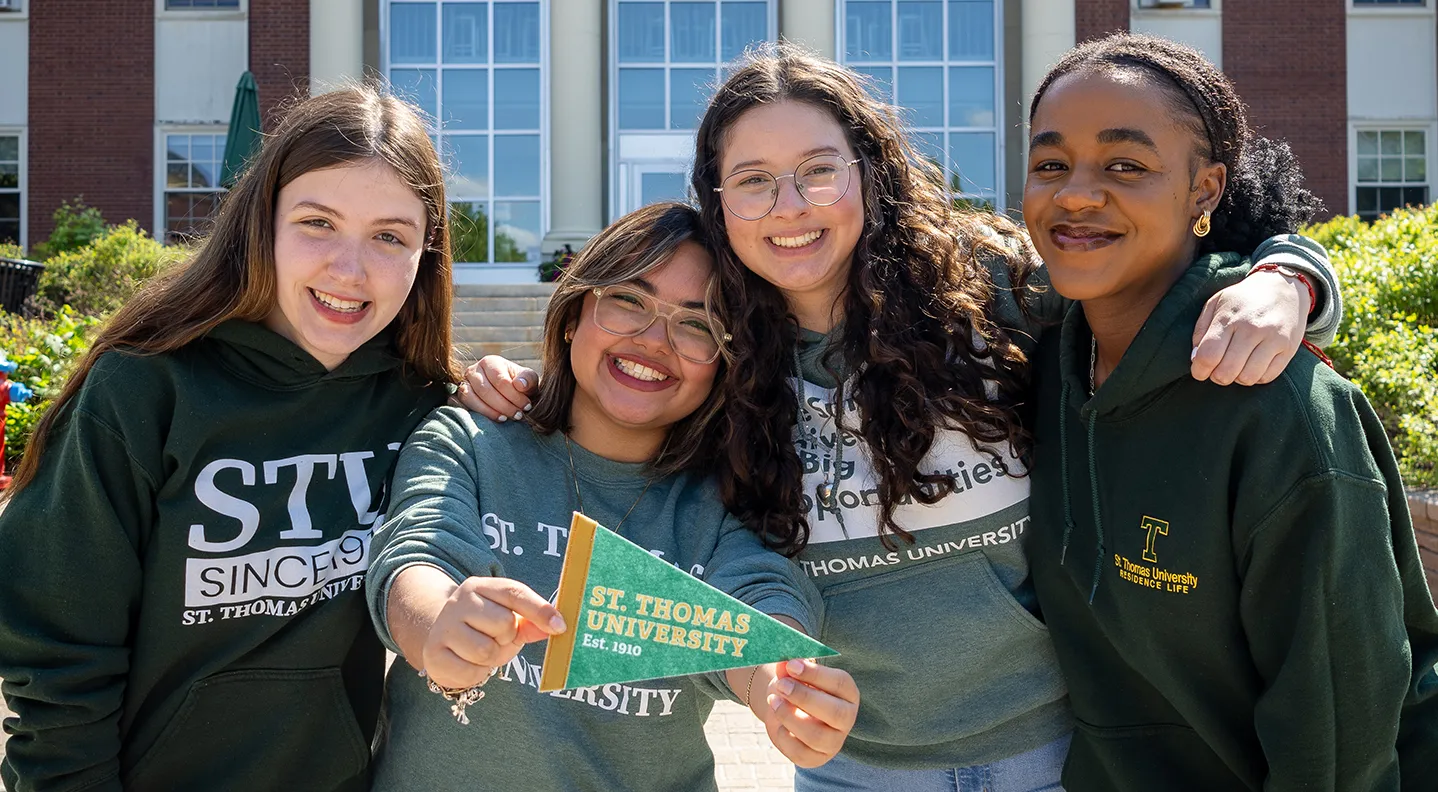 a photo of four female students on STU campus holding out a pennant for the university