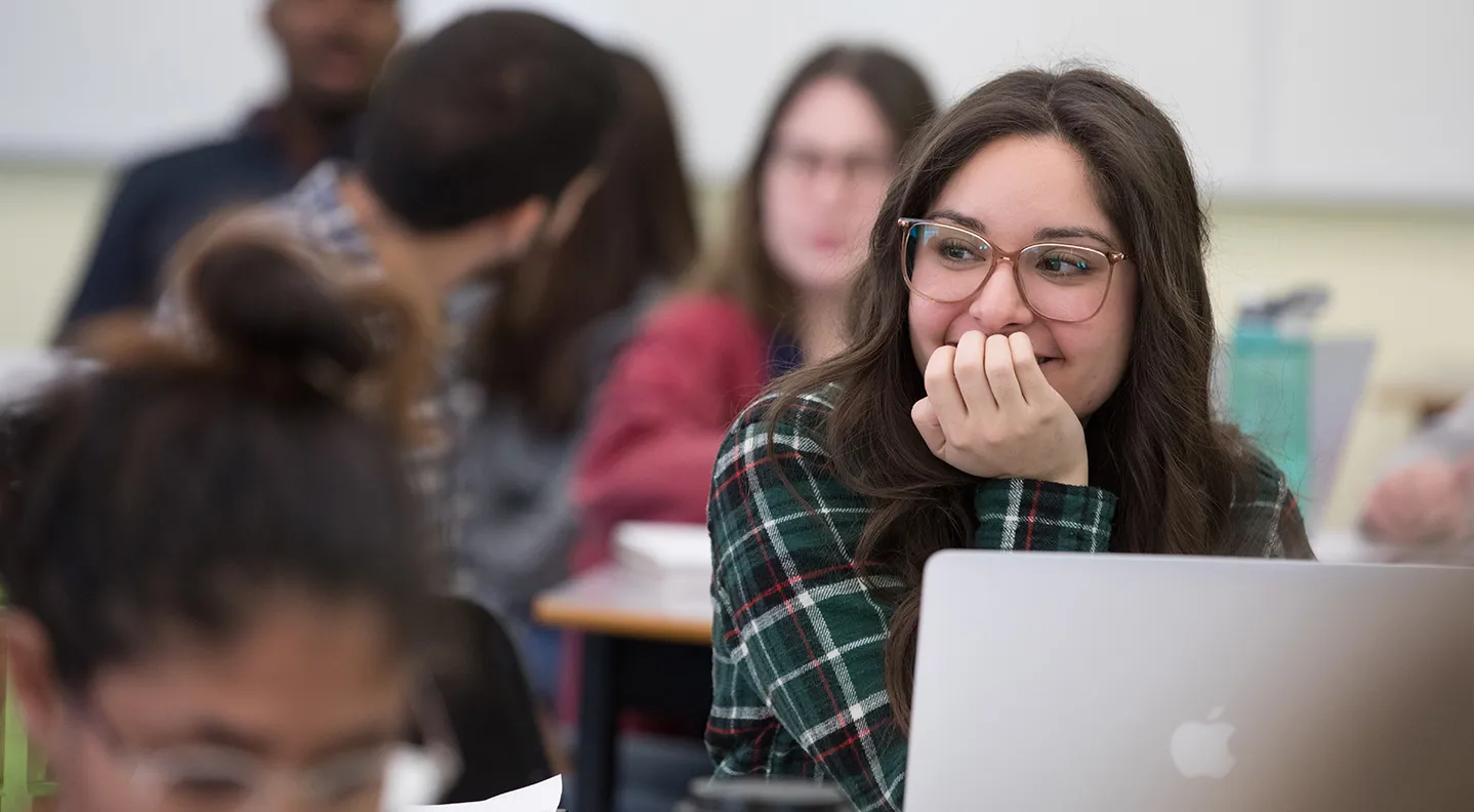 a photo of a female student sitting in class with her laptop, smiling