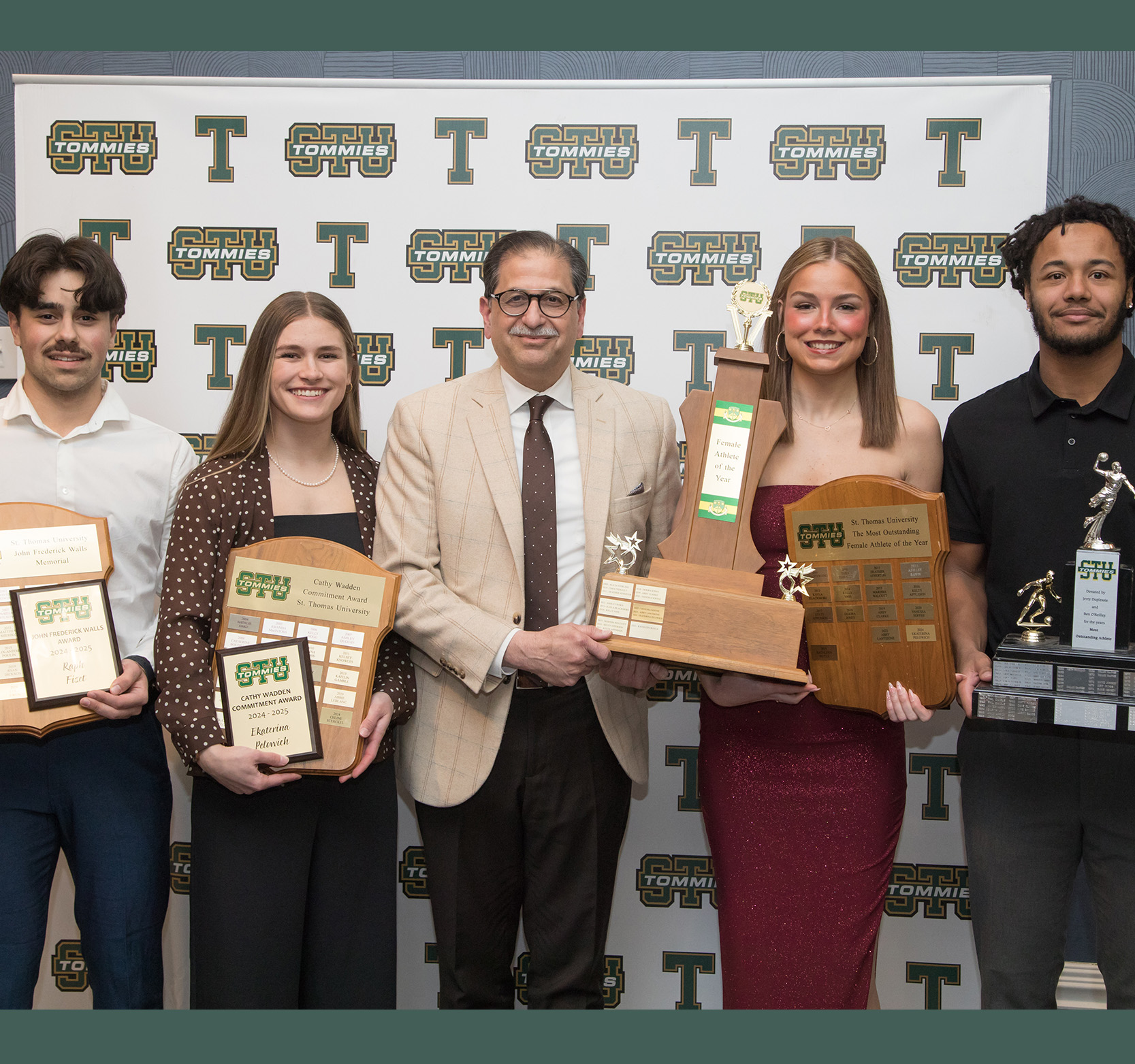 Dr. Nauman Farooqi stands with award-winning student athletes in front of a STU Tommies backdrop.