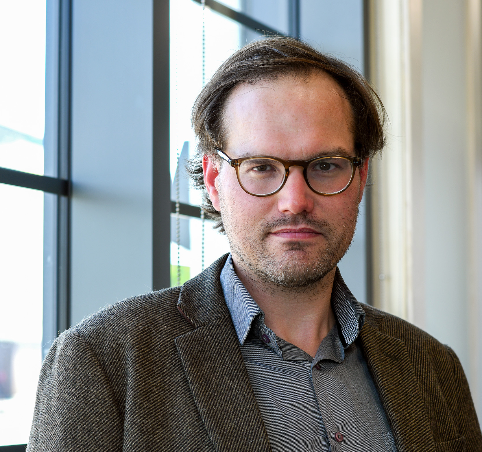 A male professor with glasses standing in front of a window