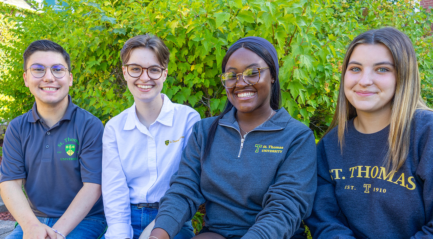 One male and three female tour ambassadors smiling on campus during summer
