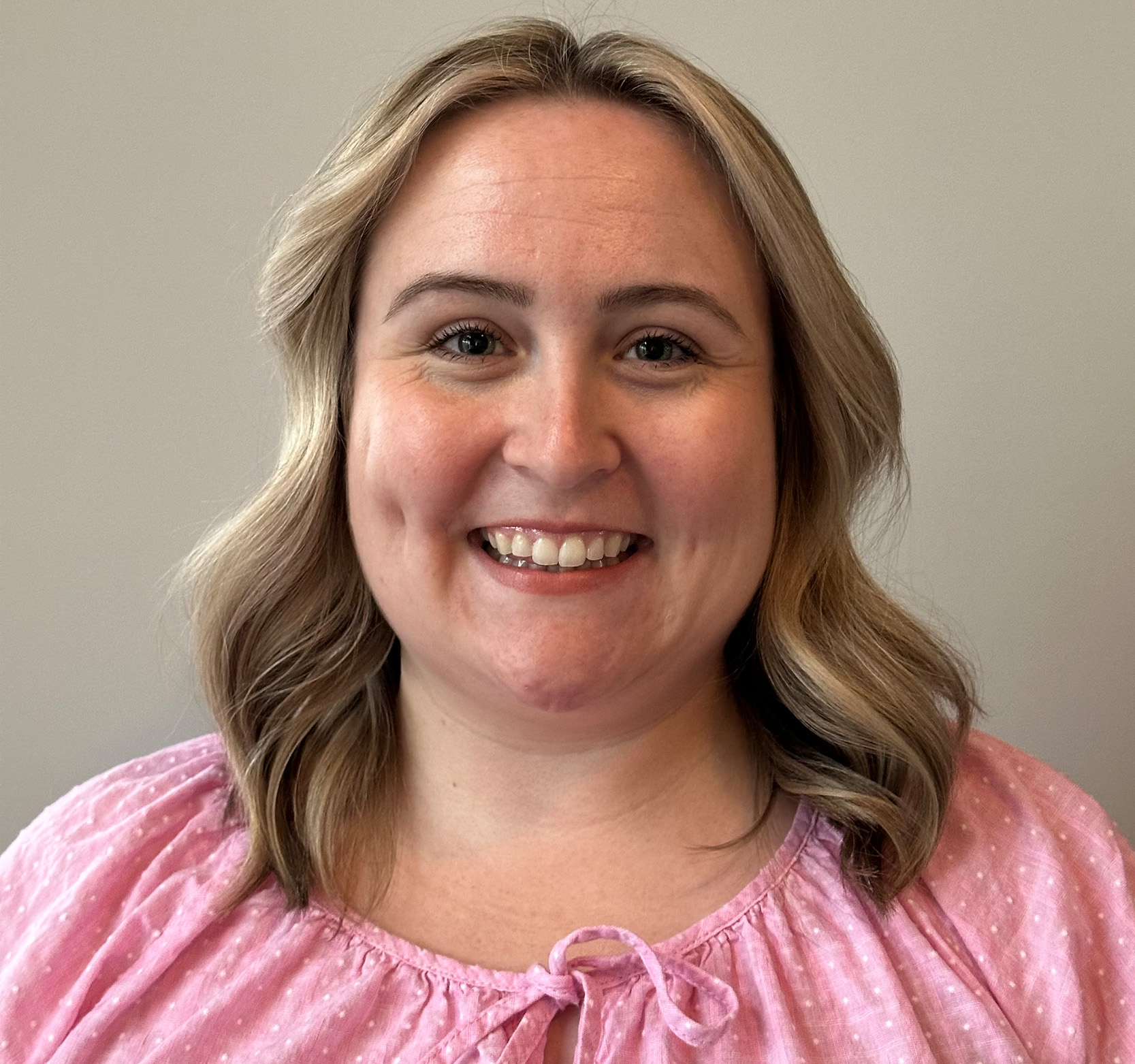 A woman with shoulder-length hair, wearing a pink top