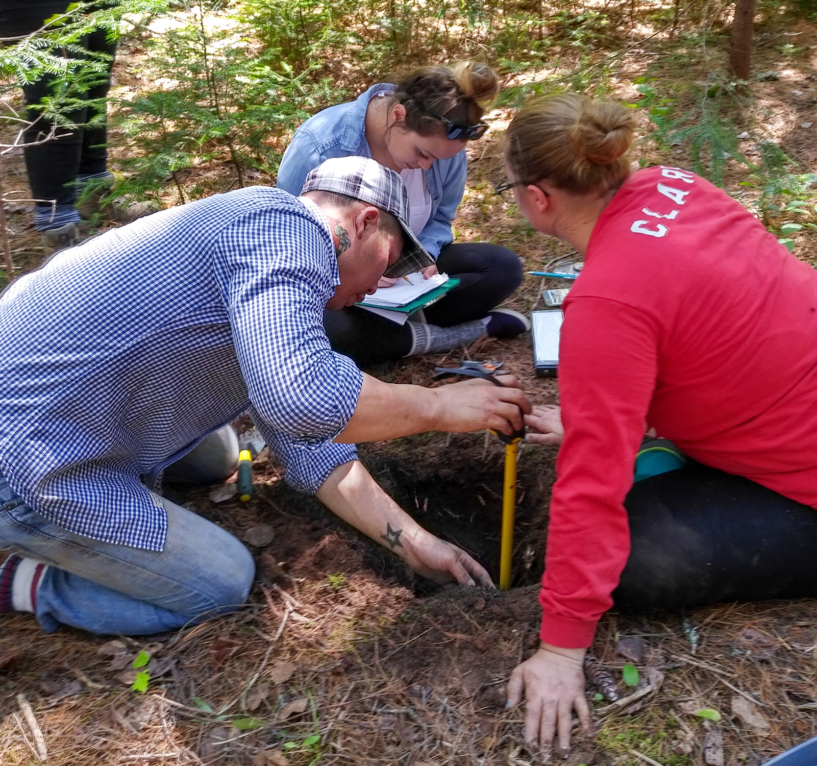 A group of students participating in archaeological fieldwork in the woods.