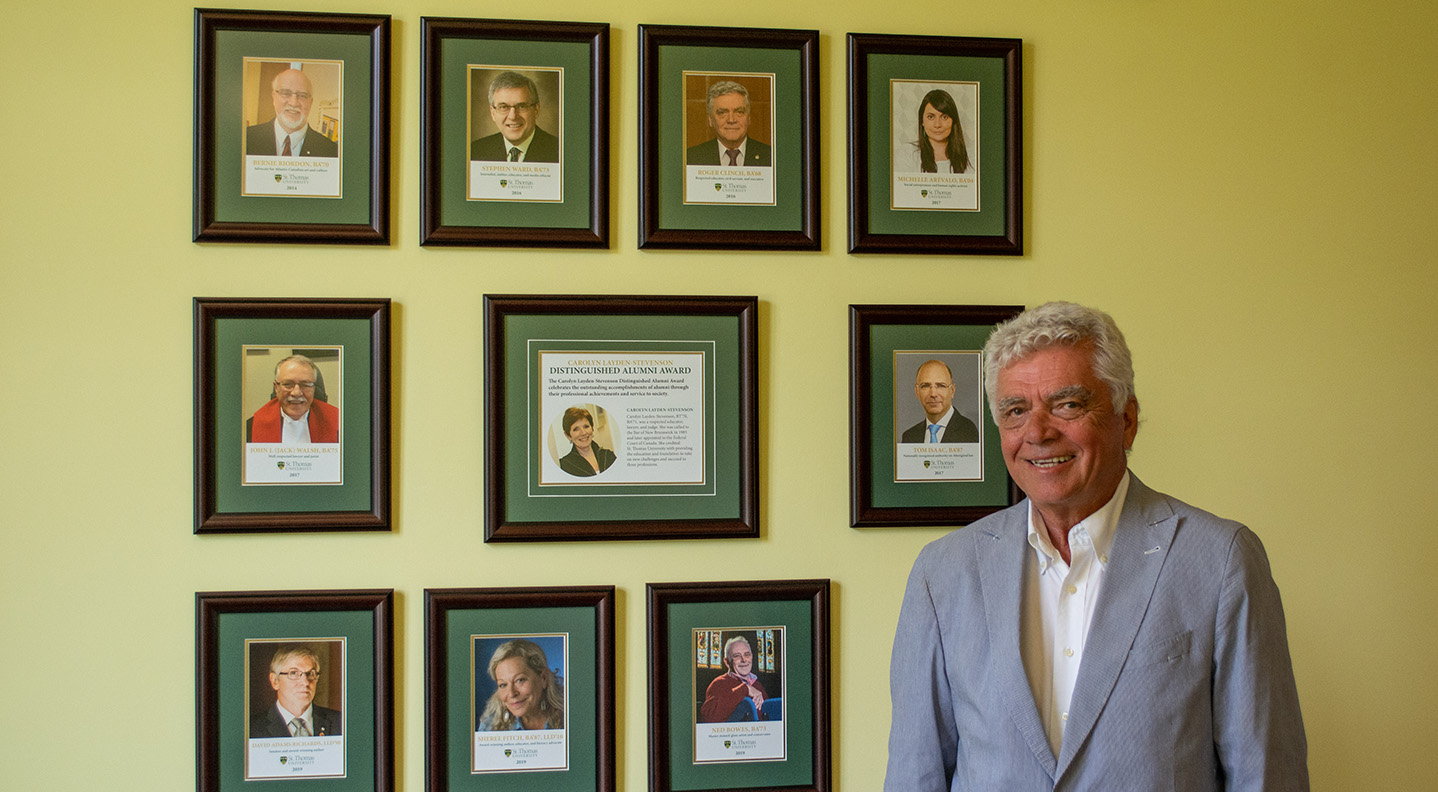 A STU alumnus stands in front of a wall showcasing past recipients of the Carolyn Layden-Stevenson Distinguished Alumni Award