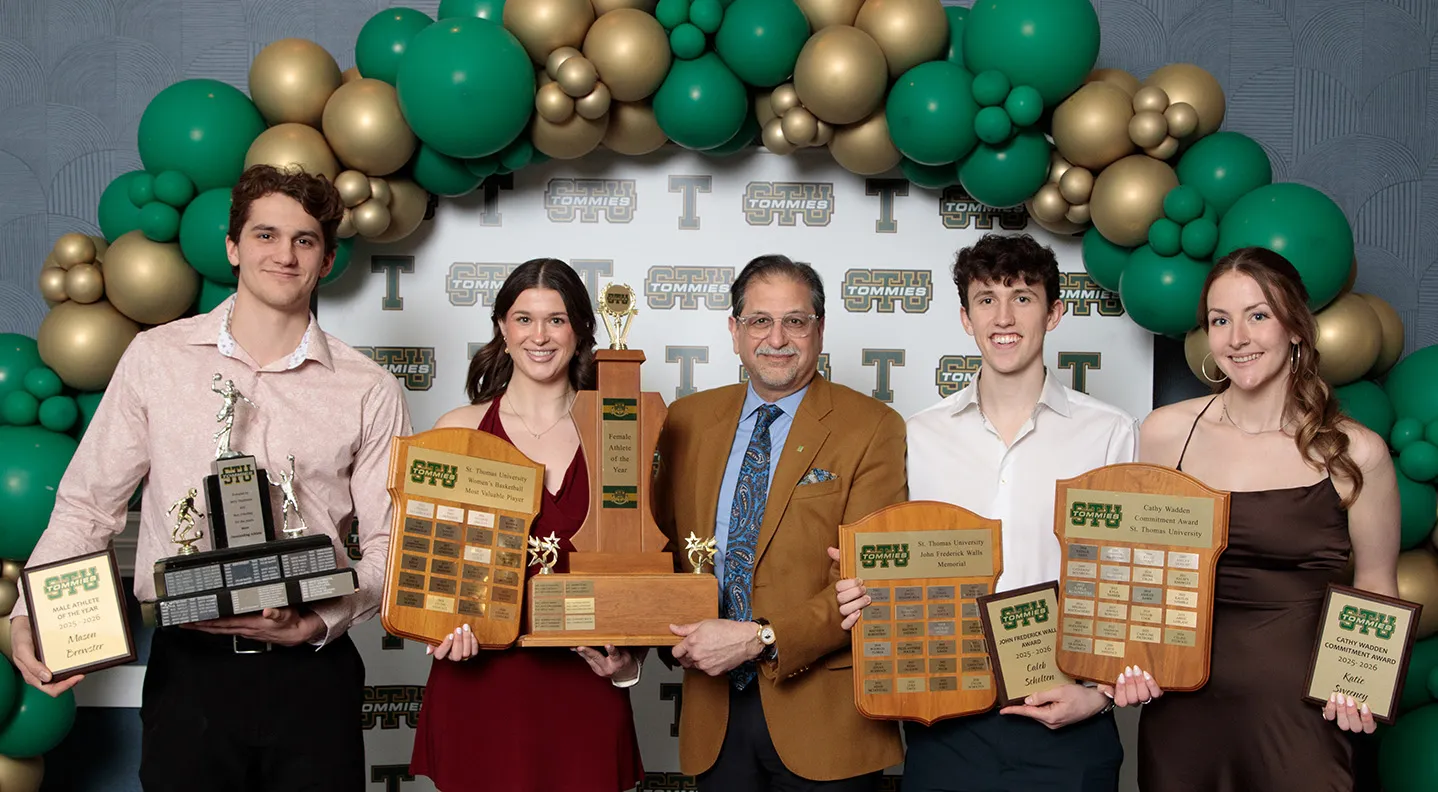 Two male students and two female students stand holding trophies and plaques with university President Dr. Nauman Farooqi