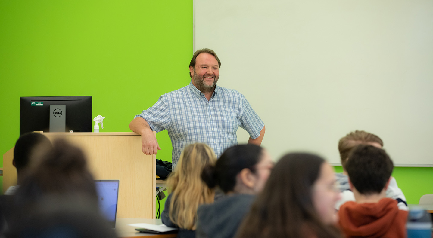 A male professor stands in front of the class