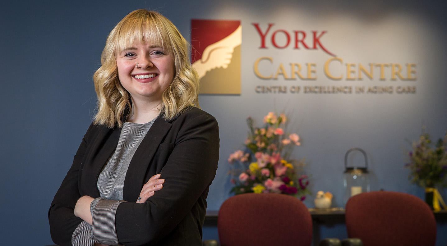 A woman stands with her arms crossed in front of a York Care Centre sign