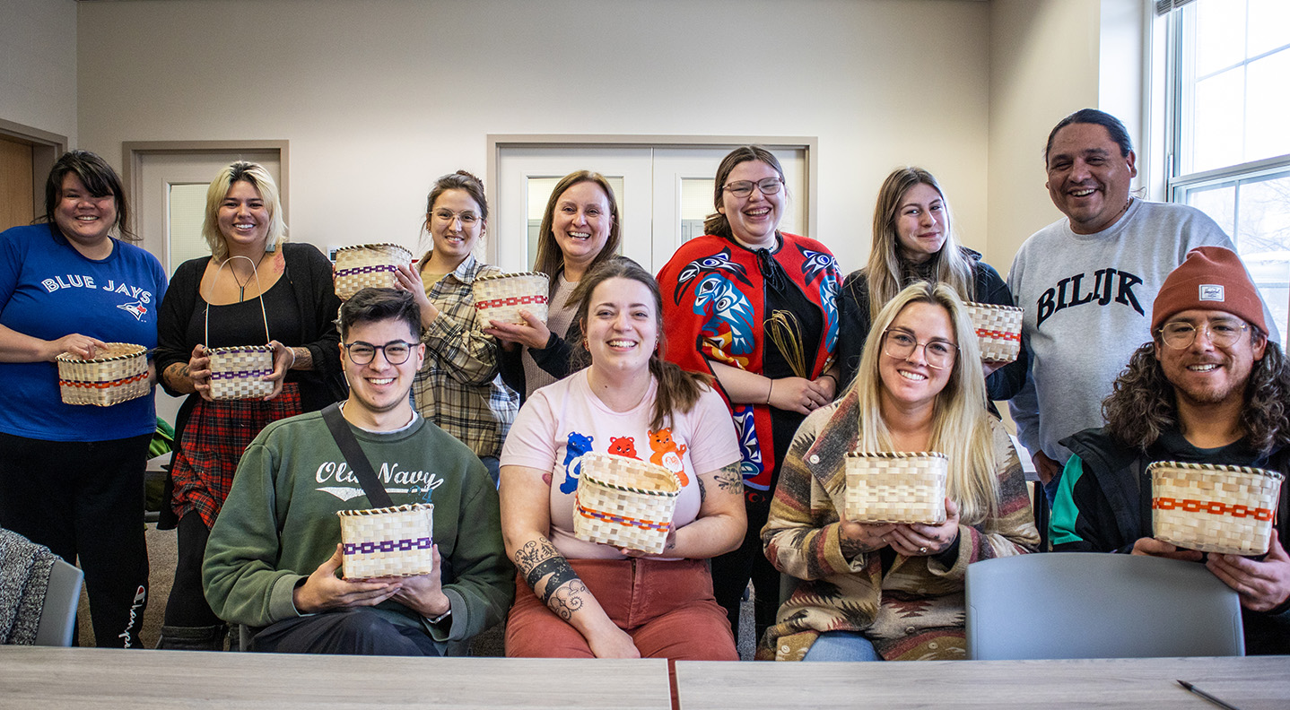 A group of students sit behind a table in the Wabanki Centre, holding their weaved baskets