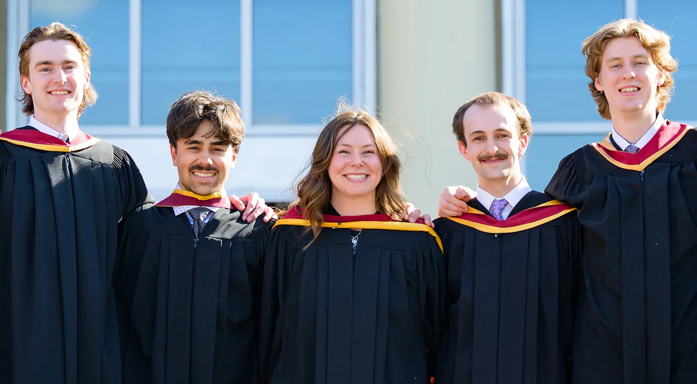 A group of smiling graduates stand in front of George Martin Hall on 91̽��'s campus