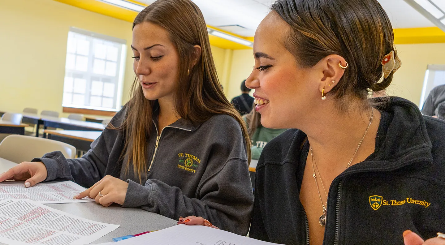 Two female students sit at a table looking at their assignment