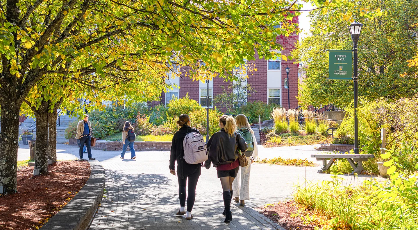 Three students walk toward George Martin Hall with their back to the camera on a sunny fall day