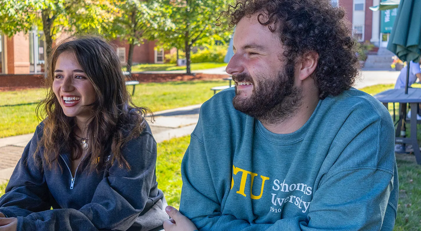 A female student and a male student sit at a picnic table in the lower courtyard on campus