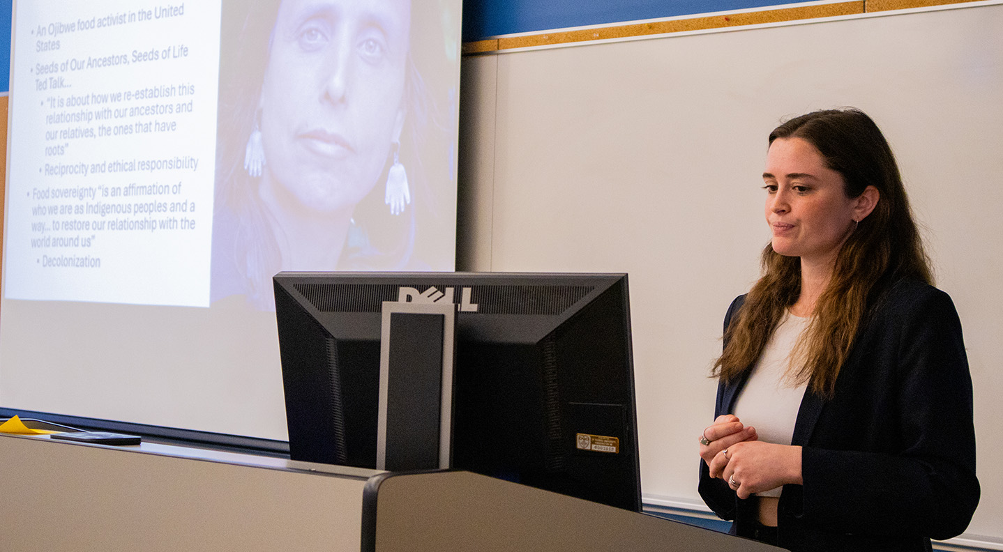 A female student stands behind a podium at the front of a classroom