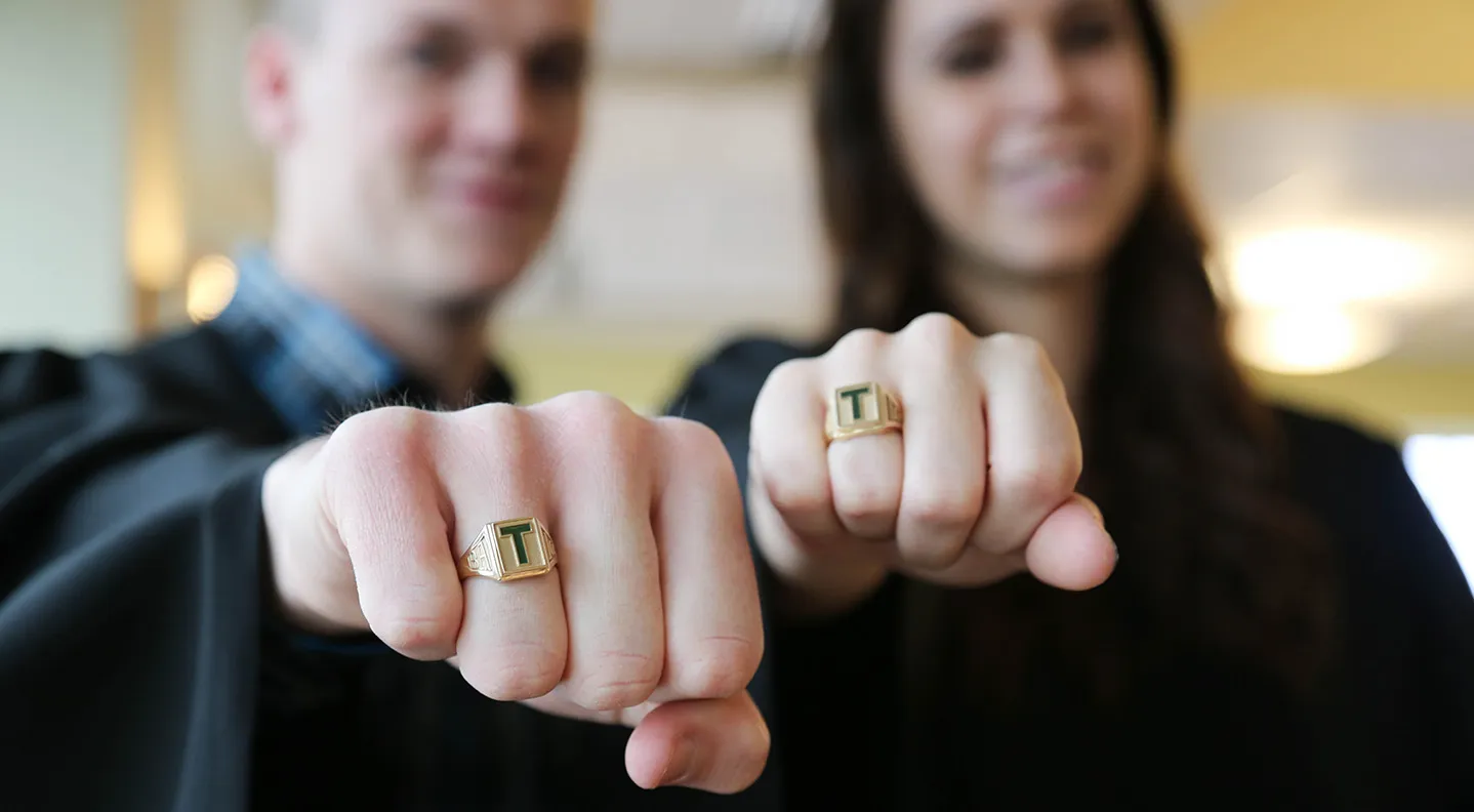 Two STU grads proudly showing off their gold T Rings