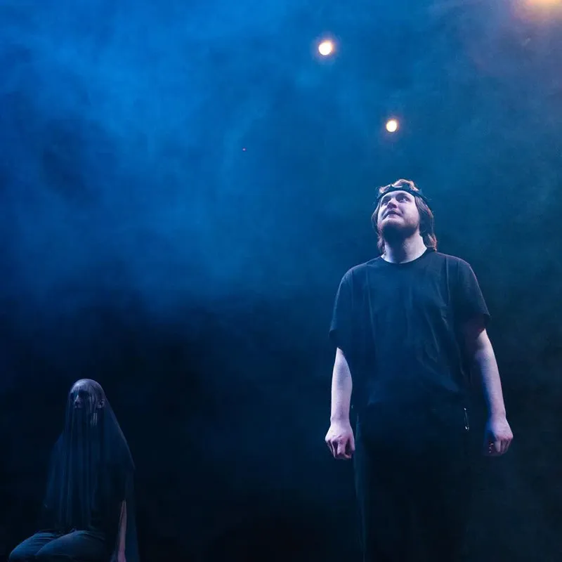 Two students stand in a dark Black Box Theatre during a performance of Macbeth