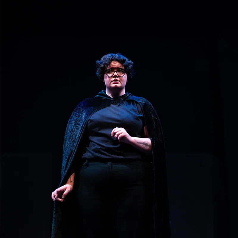 A student in costume stands under a spotlight in the Black Box Theatre