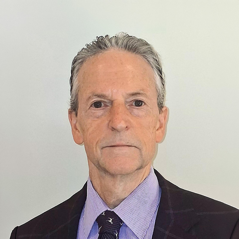 Dr. Rick Myers stands in front of a gray wall wearing a blue suit