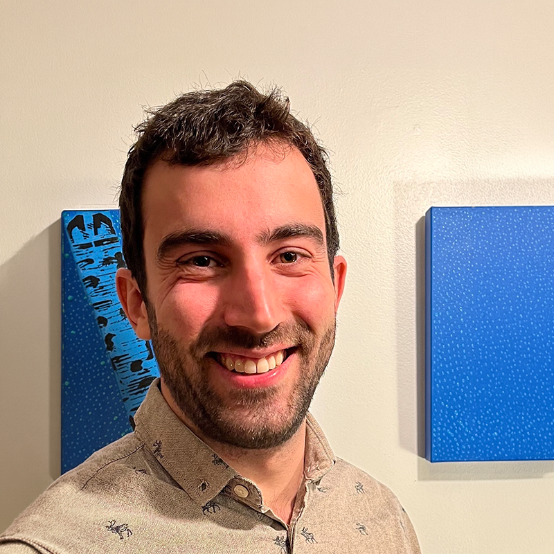 A man standing in front of a beige wall with two pieces of blue artwork.