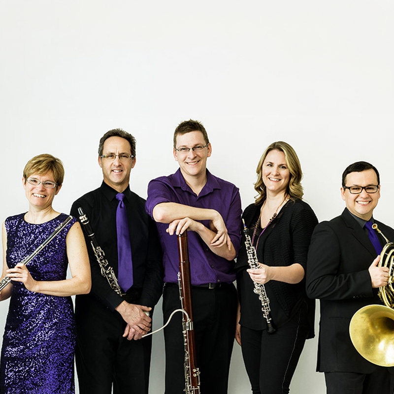 The group Ventus Machina stands holding their instruments in front of a white backdrop
