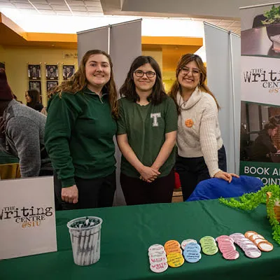 Three students manning the Writing Centre Booth