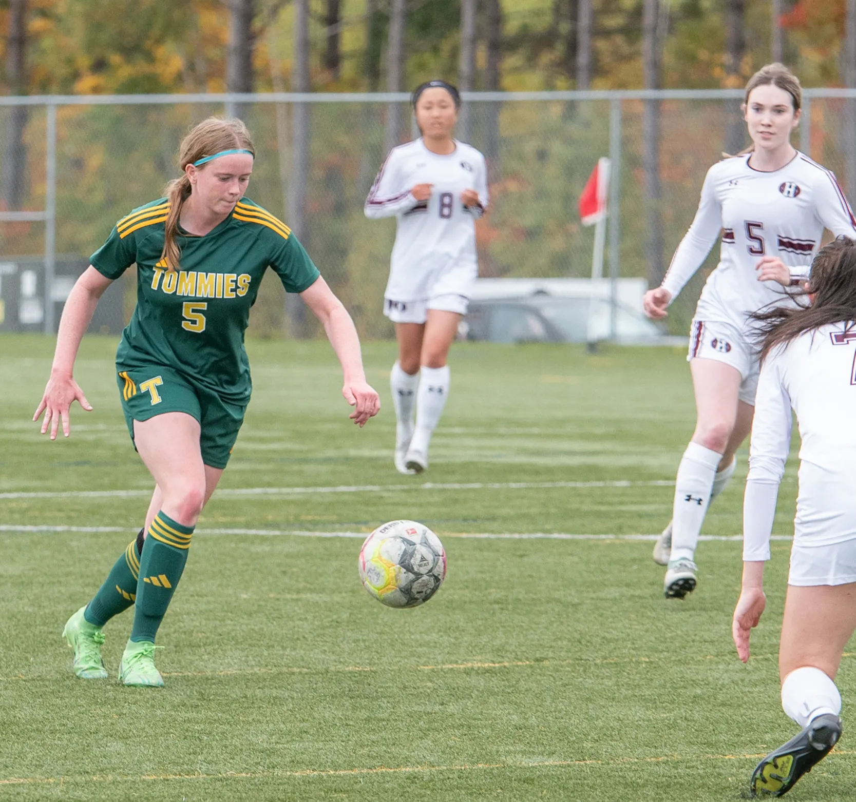 A female soccer player wearing a green Tommies jersey chases the ball on the pitch