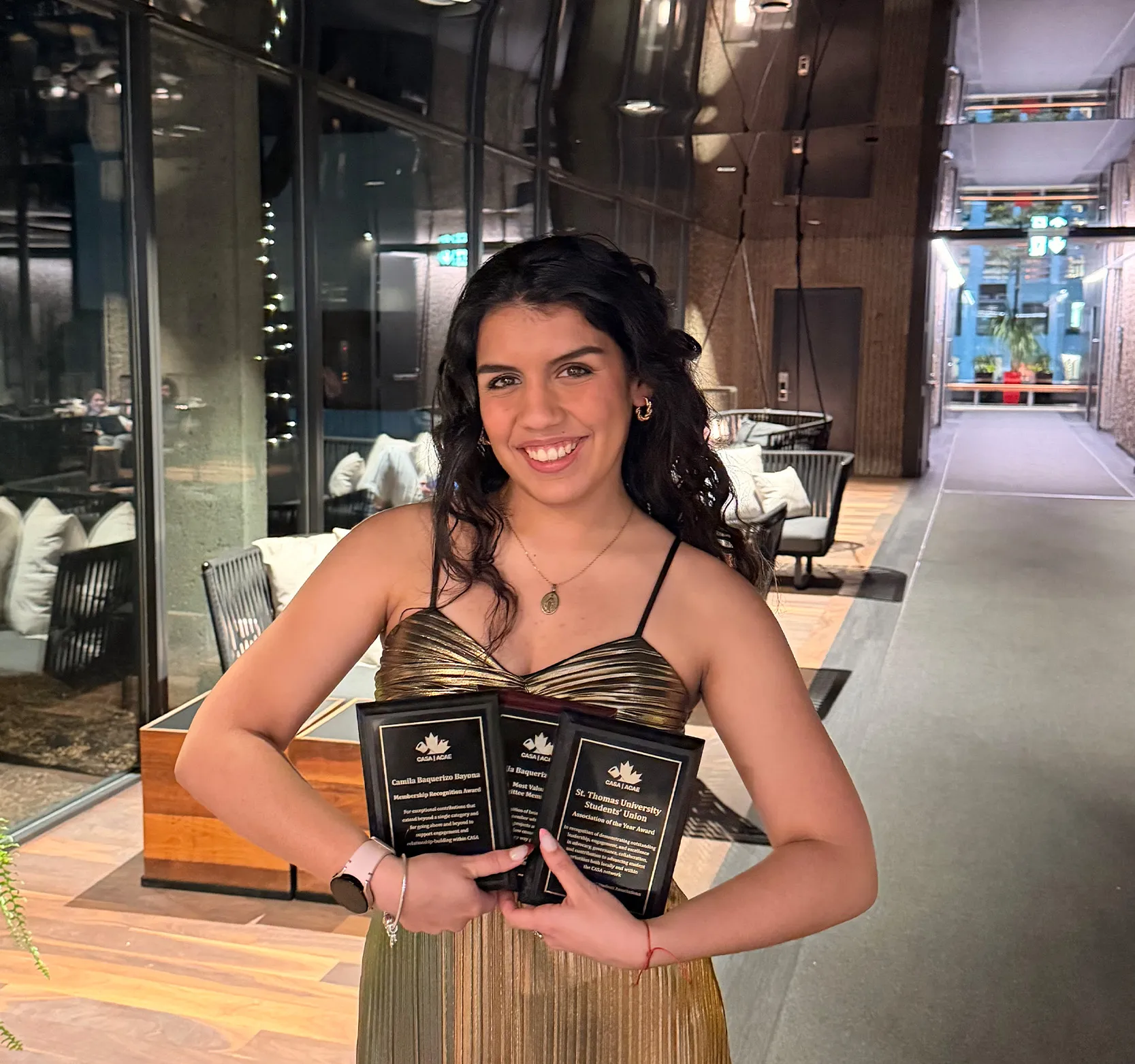 Camilla holding three plaques in hotel lobby