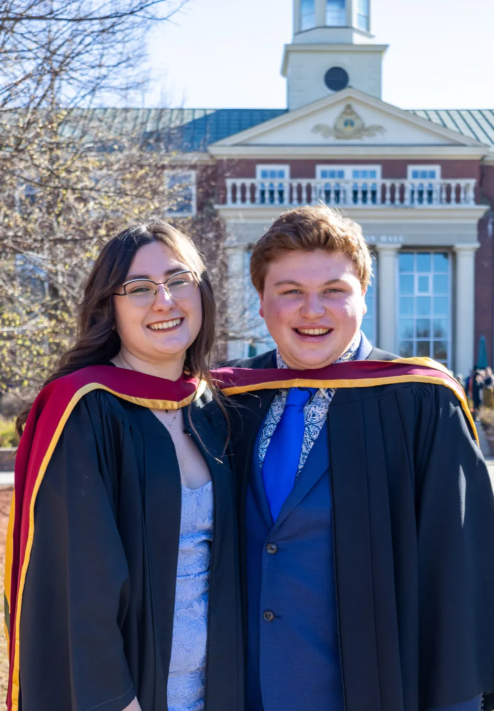 One female and male grad standing in front of GMH during Convocation Day